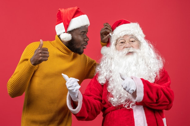 Vorderansicht des Weihnachtsmannes mit dem jungen Mann an der roten Wand