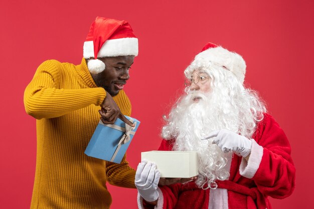 Vorderansicht des Weihnachtsmannes mit dem jungen Mann, der an der roten Wand öffnet