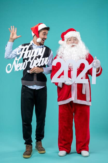 Vorderansicht des Weihnachtsmannes mit dem Mann, der glückliches neues Jahr und 2021 Bretter an der blauen Wand hält