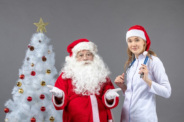 Vorderansicht des Weihnachtsmannes mit der jungen Ärztin an der grauen Wand