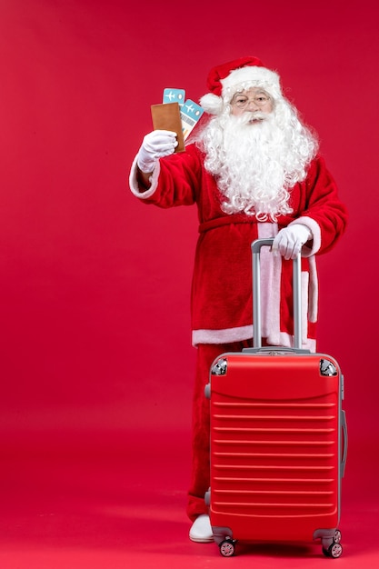 Vorderansicht des Weihnachtsmannes mit der Tasche, die Tickets hält und sich auf die Reise an der roten Wand vorbereitet