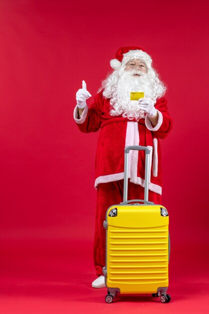Vorderansicht des Weihnachtsmannes mit gelbem Beutel, der gelbe Bankkarte an der roten Wand hält