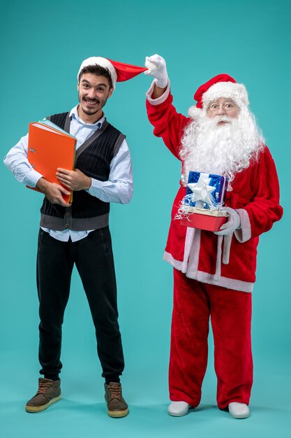 Vorderansicht des Weihnachtsmannes mit jungem Mann und präsentiert auf blauer Wand