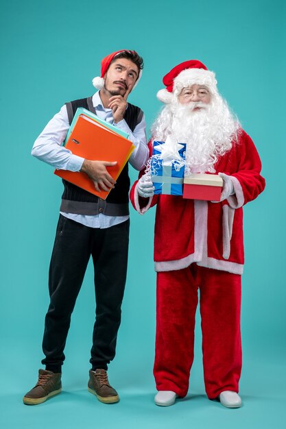 Vorderansicht des Weihnachtsmannes mit jungem Mann und präsentiert auf blauer Wand