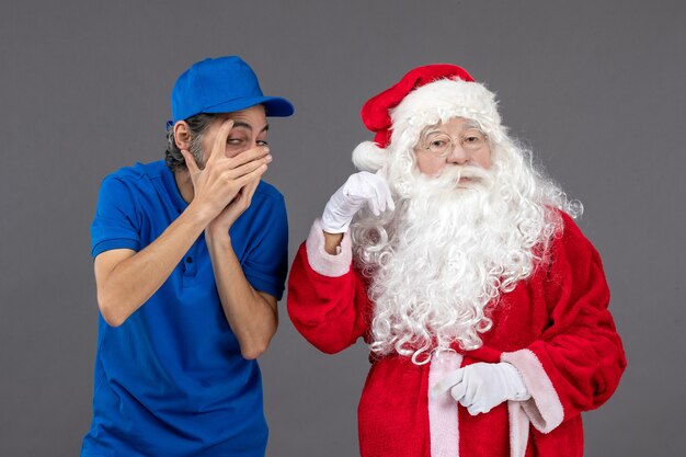 Vorderansicht des Weihnachtsmannes mit männlichem Kurier an der grauen Wand