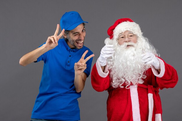 Vorderansicht des Weihnachtsmannes mit männlichem Kurier an der grauen Wand