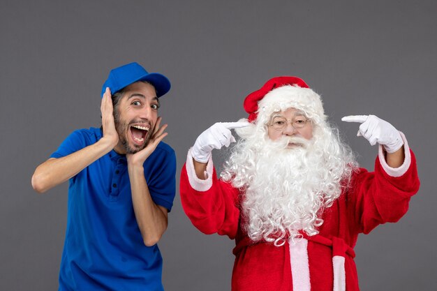 Vorderansicht des Weihnachtsmannes mit männlichem Kurier an der grauen Wand