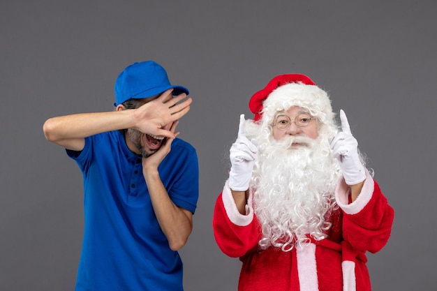 Vorderansicht des Weihnachtsmannes mit männlichem Kurier an der grauen Wand