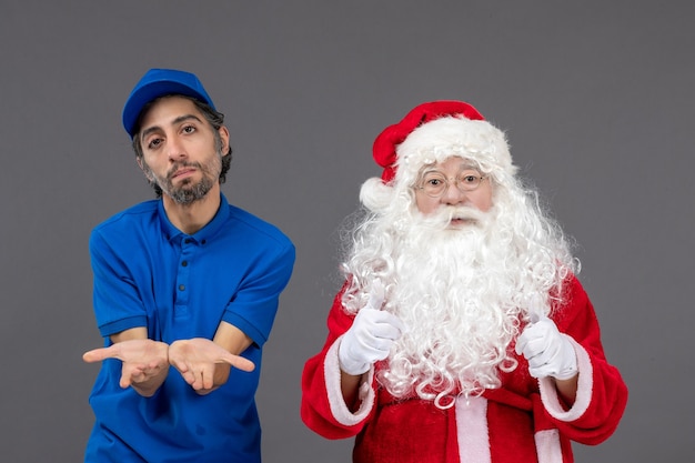 Vorderansicht des Weihnachtsmannes mit männlichem Kurier an der grauen Wand