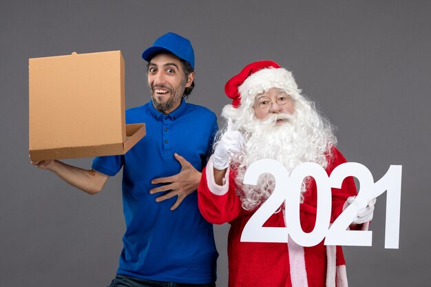 Vorderansicht des Weihnachtsmannes mit männlichem Kurier, der Nahrungsmittelbox hält und auf die graue Wand schreibt