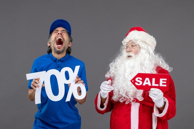 Vorderansicht des Weihnachtsmannes mit männlichem Kurier, der Verkaufsfahnen an der grauen Wand hält