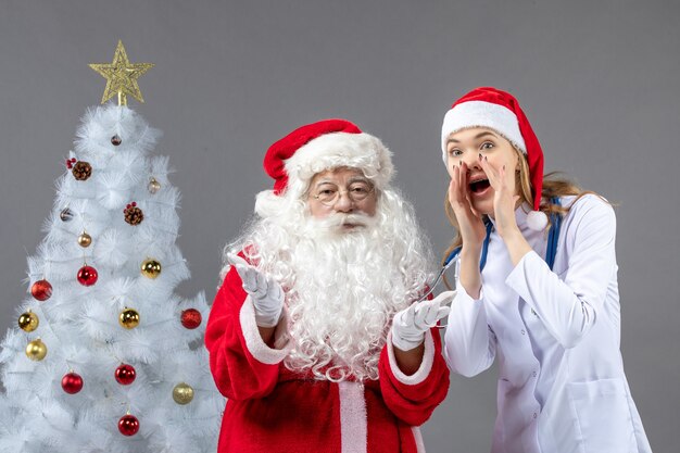 Vorderansicht des Weihnachtsmannes mit Ärztin an der grauen Wand