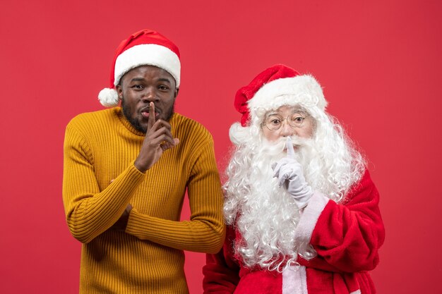 Vorderansicht des Weihnachtsmanns, der mit dem jungen Mann an der roten Wand interagiert