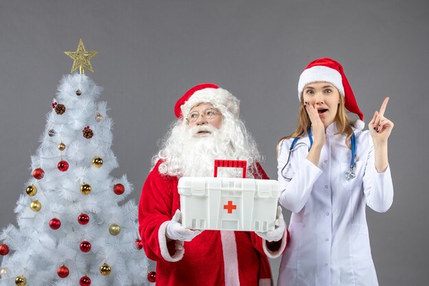 Vorderansicht des Weihnachtsmanns mit der Ärztin, die ihm Erste-Hilfe-Kasten an der grauen Wand gab