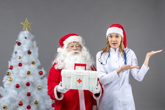 Vorderansicht des Weihnachtsmanns mit der Ärztin, die ihm Erste-Hilfe-Kasten an der grauen Wand gab