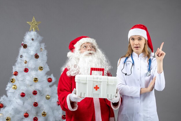 Vorderansicht des Weihnachtsmanns mit der Ärztin, die ihm Erste-Hilfe-Kasten an der grauen Wand gab