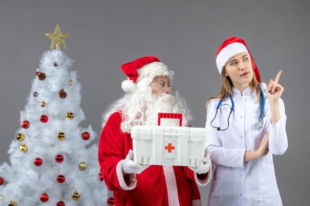 Vorderansicht des Weihnachtsmanns mit der Ärztin, die ihm Erste-Hilfe-Kasten an der grauen Wand gab