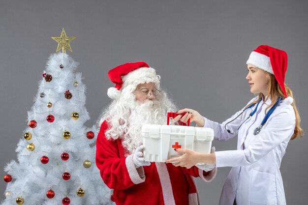 Vorderansicht des Weihnachtsmanns mit der Ärztin, die ihm Erste-Hilfe-Kasten an der grauen Wand gab