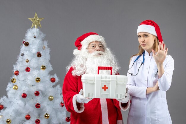 Vorderansicht des Weihnachtsmanns mit der Ärztin, die ihm Erste-Hilfe-Kasten an der grauen Wand gab