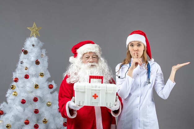 Vorderansicht des Weihnachtsmanns mit der Ärztin, die ihm Erste-Hilfe-Kasten an der grauen Wand gab