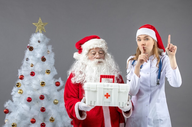 Vorderansicht des Weihnachtsmanns mit der Ärztin, die ihm Erste-Hilfe-Kasten an der grauen Wand gab