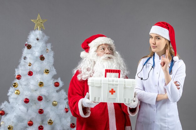 Vorderansicht des Weihnachtsmanns mit der Ärztin, die ihm Erste-Hilfe-Kasten an der grauen Wand gab