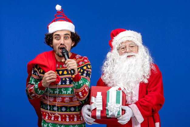 Vorderansicht des Weihnachtsmanns mit einem jungen Mann, der ein Mikrofon an der blauen Wand verwendet