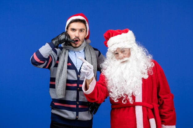 Vorderansicht des Weihnachtsmanns mit jungem Mann an der blauen Wand