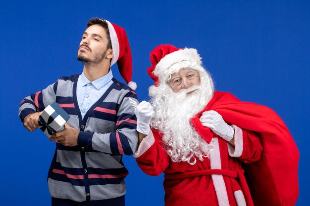 Vorderansicht des Weihnachtsmanns mit jungem Mann, der an der blauen Wand präsent ist