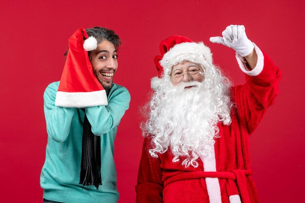 Vorderansicht des Weihnachtsmanns mit jungem Mann, der auf der roten Wand steht