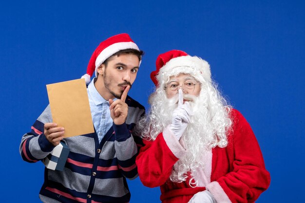 Vorderansicht des Weihnachtsmanns mit jungem Mann, der Brief an der blauen Wand hält