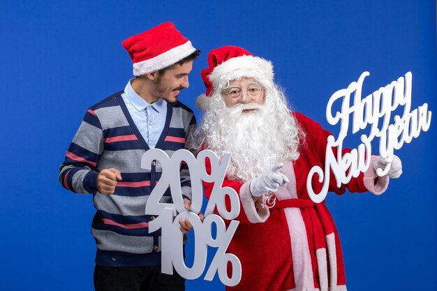 Vorderansicht des Weihnachtsmanns mit jungem Mann, der ein frohes neues Jahr und Prozentschriften an der blauen Wand hält