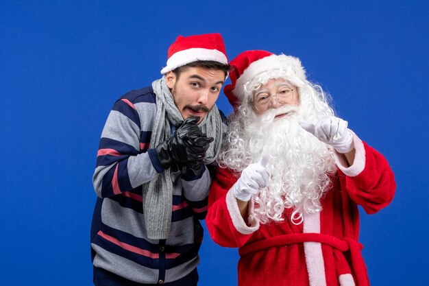 Vorderansicht des weihnachtsmanns mit jungem mann, der vor kälte an blauer wand zittert