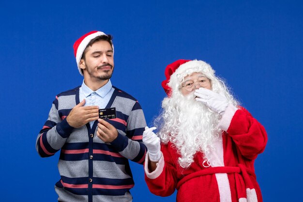 Vorderansicht des Weihnachtsmanns mit jungem Mann mit Bankkarte an der blauen Wand