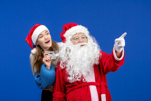 Vorderansicht des Weihnachtsmanns mit junger hübscher Frau an der blauen Wand