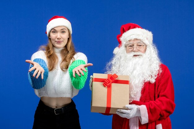 Vorderansicht des Weihnachtsmanns zusammen mit der Frau, die Geschenk an der blauen Wand hält