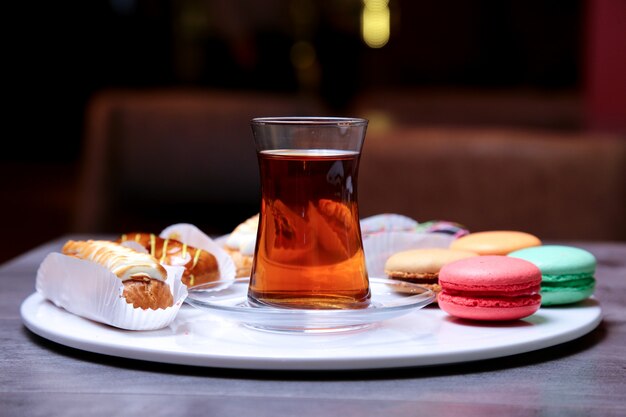 Vorderansicht Desserts Schokolade Karamell und Sahne Eclairs mit Macarons Kekse auf einem Teller mit Tee in einem Glas Armouda