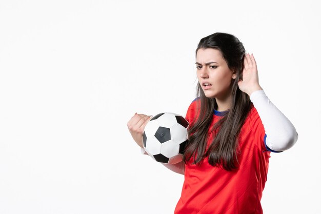 Vorderansicht, die junge Frau in Sportkleidung mit Fußball hört