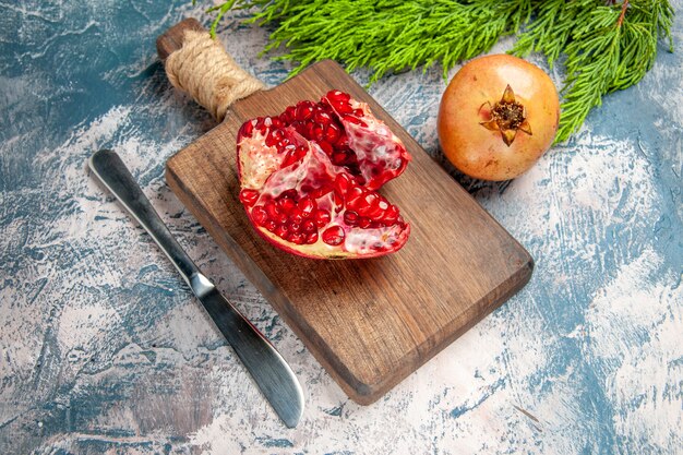 Vorderansicht ein geschnittener Granatapfel auf Schneidebrett Granatapfelmesser auf blau-weißem Hintergrund