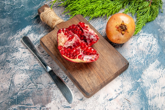 Vorderansicht ein geschnittener Granatapfel auf Schneidebrett Granatapfelmesser auf blau-weißem Hintergrund