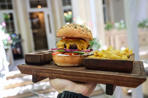 Kostenloses Foto vorderansicht ein mann, der ein tablett mit fleischburgern mit roten zwiebeln und pommes mit saucen hält