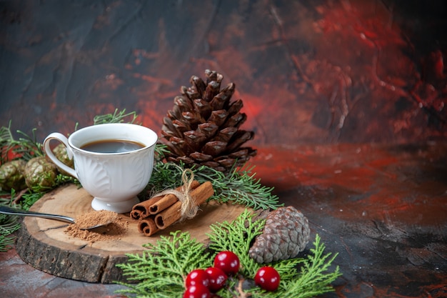 Vorderansicht eine tasse tee auf holzbrett zimtstangen kiefernzapfen auf dunkel