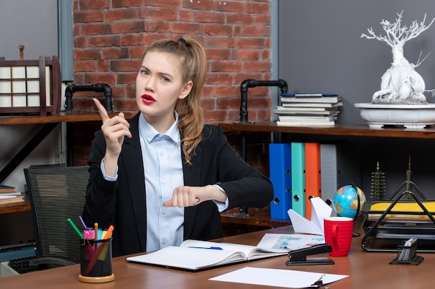 Vorderansicht einer emotional schockierten Frau, die an einem Tisch sitzt und im Büro nach oben zeigt