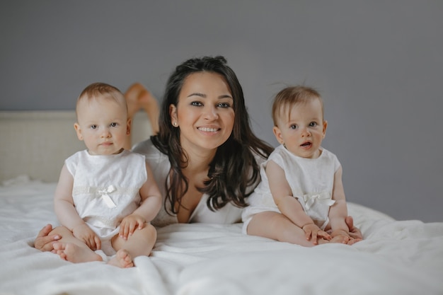 Vorderansicht einer glücklich lächelnden alleinerziehenden Mutter mit Baby-Zwillingsmädchen zu Hause.
