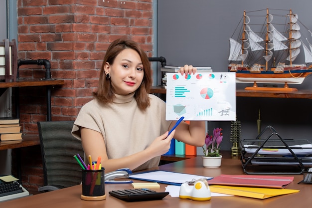 Vorderansicht einer hübschen Frau, die Diagramme zeigt, die im Büro arbeiten