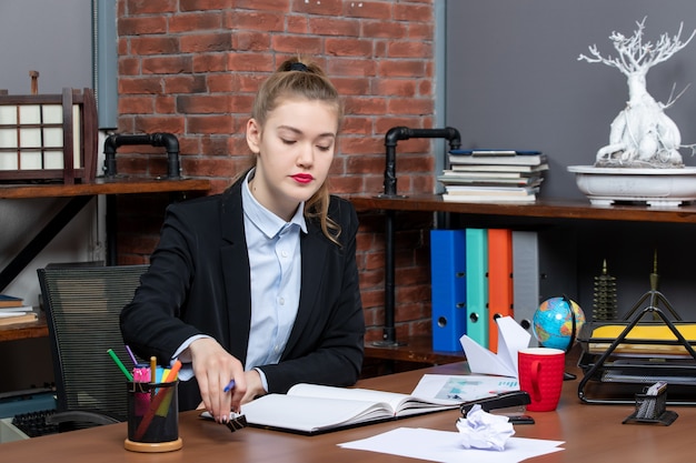 Kostenloses Foto vorderansicht einer jungen dame, die an einem tisch sitzt und ihre notizen im notizbuch im büro liest