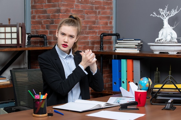 Vorderansicht einer jungen Frau, die an einem Tisch sitzt und eingewickeltes Papier im Büro hält