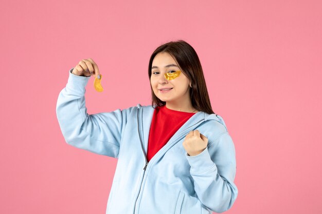 Vorderansicht einer jungen Frau, die eine Gesichtsmaske an einer rosa Wand macht