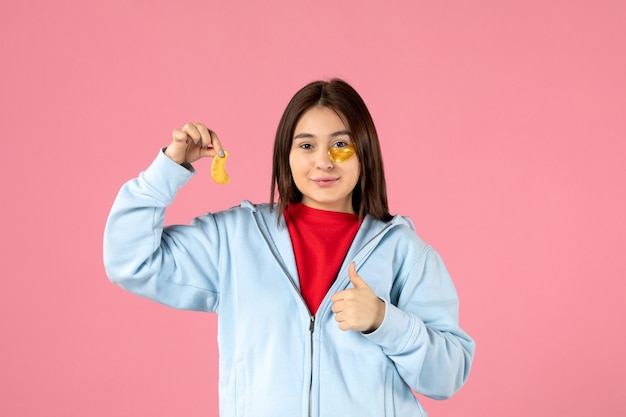 Vorderansicht einer jungen Frau, die eine Gesichtsmaske an einer rosa Wand macht