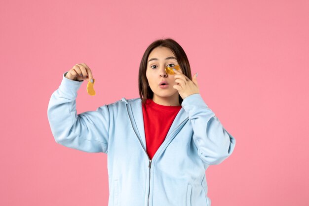 Vorderansicht einer jungen Frau, die eine Gesichtsmaske an einer rosa Wand macht